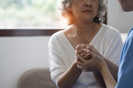 Happy patient is holding caregiver for a hand while spending time together. Elderly woman in nursing home and nurse.の写真素材
