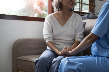 Happy patient is holding caregiver for a hand while spending time together. Elderly woman in nursing home and nurse.の写真素材
