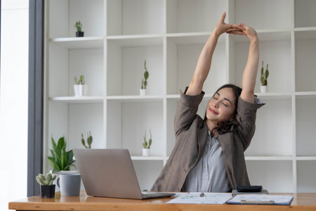 Asian businesswoman stretches her arms to relax her tired muscles from working at her desk all day at the office.の写真素材