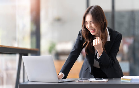 Beautiful asian woman using laptop computer, exciting and celebrating with good news of business successful. Small business startup concept.の写真素材
