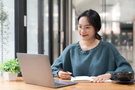 Beautiful women student studying online takes notes on her laptop to gather information about her work smiling face and a happy study posture.の写真素材