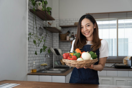 Portrait of young happy woman wearing appron standing in the kitchen room, prepares cooking healthy food from fresh vegetables and fruits.の写真素材
