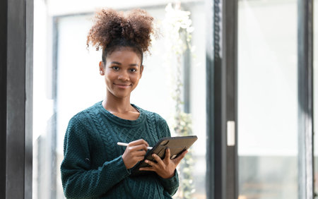 Shot of smiling young entrepreneur woman using her digital tablet while standing next to the window...