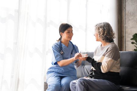 Young caregiver helping senior woman walking. Nurse assisting her old woman patient at nursing home. Senior woman with walking stick being helped by nurse at home.の写真素材