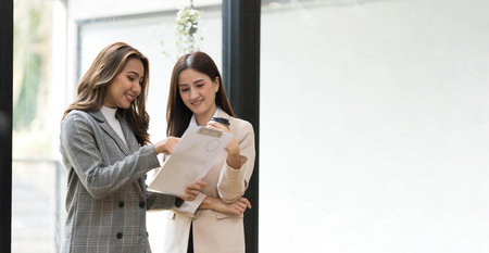 Two Asian businesswomen discussing, sharing their business ideas, reviewing financial report together.の写真素材