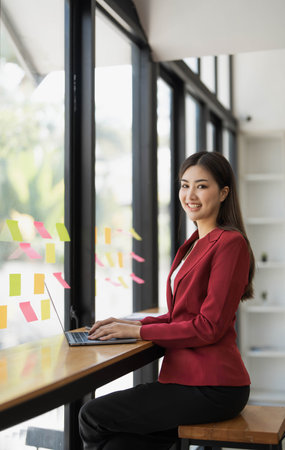 Charming Asian businesswoman sitting in the office with a digital laptop computer. Excited Asian businesswoman raising hands to congratulate while working in a modern office,の写真素材