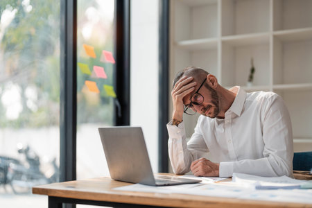 Young unhappy man office worker feeling bored at work, looking at laptop with demotivated face...