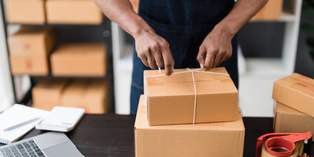 Photo of young entrepreneur man packing he goods while sitting in table comfortable sitting room as background. Shipping, Shopping online, Small business entrepreneur, SME, freelance.の写真素材