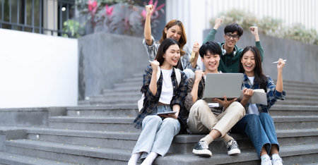 Group of cheerful Asian college students sitting on stairs, showing fists, celebrating triumphの写真素材