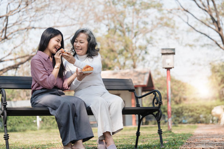 Happy adult granddaughter and senior grandmother having fun enjoying talk sit with green nature. in parkの写真素材