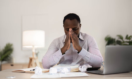 Concentrated business african american man working from home, sitting at work desk, using laptop, looking at laptop thoughtfully, hands near face, thinking about financial business plan or new startupの写真素材