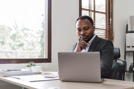 Stressed business man sitting at office workplace. Tired and overworked black man. Young african american exhausted men in stress working on laptop computerの写真素材