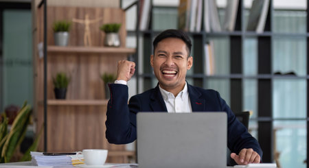 Happy young businessman looking at laptop computer in office, Excited asian man working at his workplace at modern co-working, successful peopleの写真素材