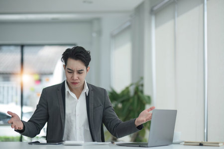 Happy satisfied millennial man using laptop at office workplace, working from home, reading message with good news, thinking, looking at screen, watching online webinar, training, making paymentの写真素材