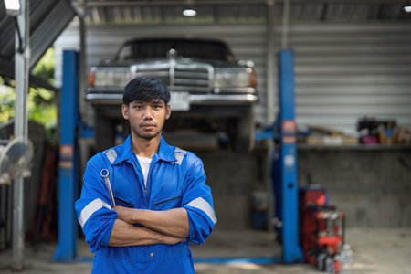 Portrait Shot of a Handsome Mechanic Working on a Vehicle in a Car Service. Professional Repairman is use a Ratchet Underneath the Car. Modern Clean Workshop.の写真素材