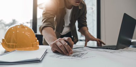 Engineers holding a pen pointing to a building and drawing outlay construction plan as guide for builders with details.の写真素材