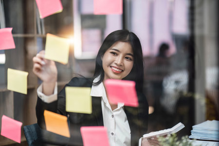 businesswoman write tasks creative ideas and planning on sticky post it note on glass wall.project...