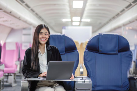Female passenger sitting on plane while working on laptop computer with simulated space using on board wireless connectionの写真素材