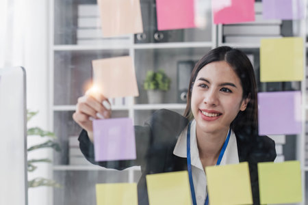 Young businesswoman creative team using post  notes in glass wall to writing strategy business plan to development grow to success.の写真素材