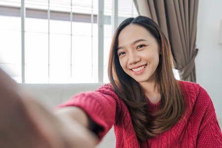 Satisfied asian woman relaxing on comfortable couch, using laptop at home, happy girl chatting with friends in social network, spending lazy weekend, watching movie, shopping online, writing emailの写真素材