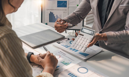 Two business people talk project strategy at office meeting room. Businessman discuss project planning with colleague at modern workplace while having conversation and advice on financial data report.の写真素材