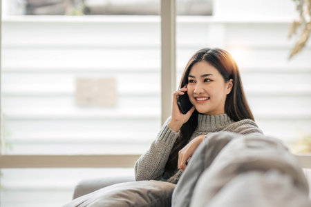 Happy casual beautiful woman is talking on a phone sitting on a sofa at home.の写真素材