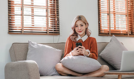 Young woman using laptop while sitting on comfortable sofa, homeの写真素材