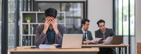 Focused serious professional using laptop in office lobby. Young asian man using laptop in background. Wireless technology conceptの写真素材