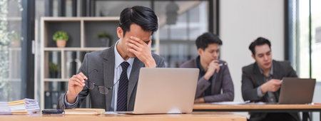 Focused serious professional using laptop in office lobby. Young asian man using laptop in background. Wireless technology conceptの写真素材