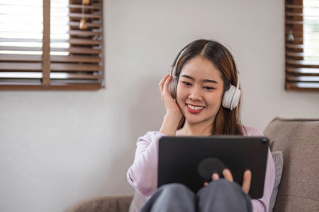 beautiful asian young woman wear casual sit on couch using computer laptop entertain with social media relax smile and laughing.Freelance woman working online sale marketing. Shopping online at homeの写真素材