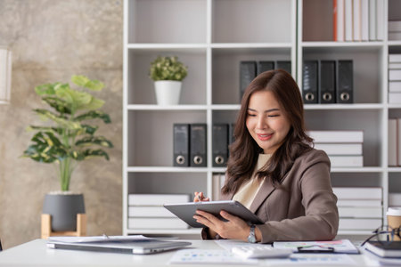 Cheerful business lady working on laptop in office, Asian happy beautiful businesswoman in formal suit work in workplace. Attractive female employee office worker smile.の写真素材