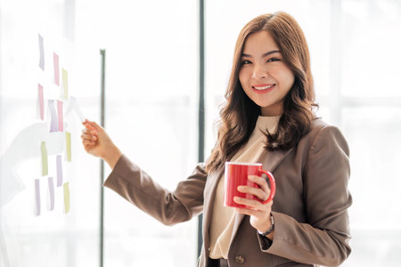 Young smiley attractive, businesswoman using sticky notes in glass wall to writing strategy business plan to development grow to successの写真素材