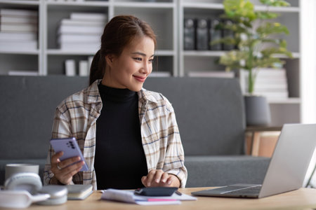 Beautiful and inspired Asian woman working on her tasks on laptop in a living room on the weekend.の写真素材