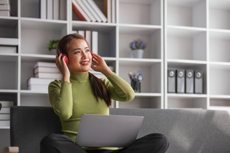 Relaxed Asian woman enjoys listening to music on her free time in a living room. Hobby and leisure...