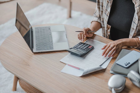Close-up image of a woman using calculator, calculating money, managing household expenses and taxes in a living room.の写真素材