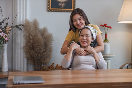 Portrait of a beautiful young Asian woman smiling and hugging her middle aged mom or grandmother, spending time at home together. Happy family bonding conceptの写真素材