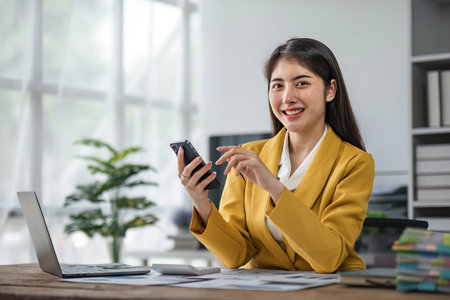 Young busy asian business woman talking on phone working in modern office. Asian businesswoman company sales client manager wearing suit making call on cellphone sitting at workplace.の写真素材