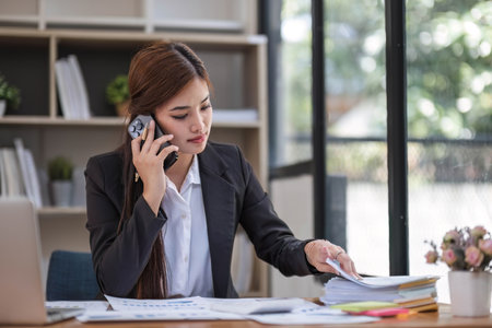 Asian businesswoman in formal suit in office happy and cheerful during using smartphone and workingの写真素材