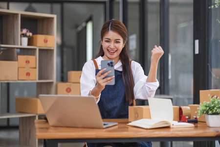 Startup SME small business entrepreneur of freelance Asian woman using a smartphone with box Cheerful success Asian woman her hand lifts up online marketing packaging box and delivery SMEの写真素材