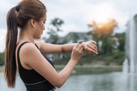 Close-up image of a beautiful and sporty Asian woman in sportswear checking her calories burned and running miles on her smartwatch after a run outdoors.の写真素材