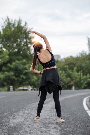 Back view, A sporty Asian woman in sportswear is stretching her body and warming up before running on the street in the park.の写真素材