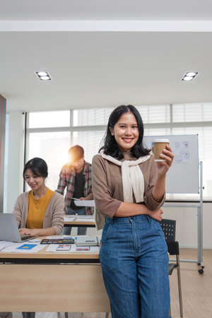 A focused young Asian female marketing assistant is working on her work on her laptop at her desk while her coworkers are working in the room.の写真素材