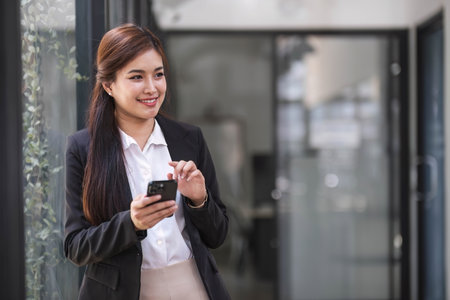 Charming Asian woman with a smile standing holding papers and mobile phone at the office.の写真素材