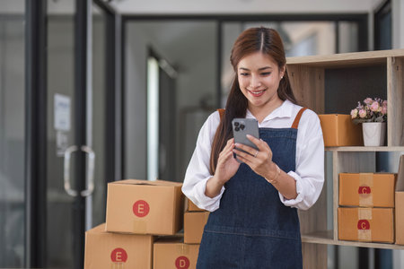 Startup SME small business entrepreneur of freelance Asian woman using a smartphone with box Cheerful success Asian woman her hand lifts up online marketing packaging box and delivery SMEの写真素材