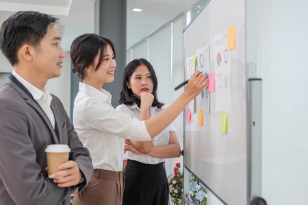Casual creative happy two smile asian business people plan strategy analysis and brainstorm putting sticker note to share idea for startup project on white board at modern officeの写真素材