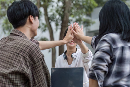 A group of happy young Asian college student putting their hands together while sitting in the campuss park. cheer up, celebrating, teamwork, best friends conceptの写真素材