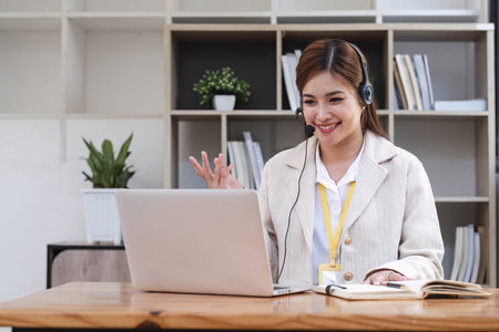Asian call center with headset and microphone working on her laptop. Female operator provide exceptional customer service. Supportive call center agent helping customer on inquiry. Enthusiasticの写真素材