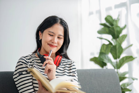 Young asian woman with headphones relaxing at home. listening to music. sitting on cozy sofa wearing...