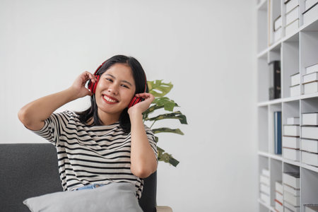 Young asian woman with headphones relaxing at home. listening to music. sitting on cozy sofa wearing headphoneの写真素材