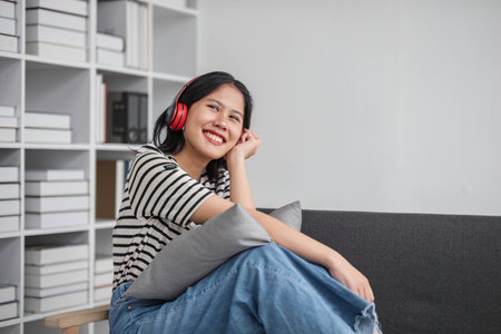 Young asian woman with headphones relaxing at home. listening to music. sitting on cozy sofa wearing headphoneの写真素材